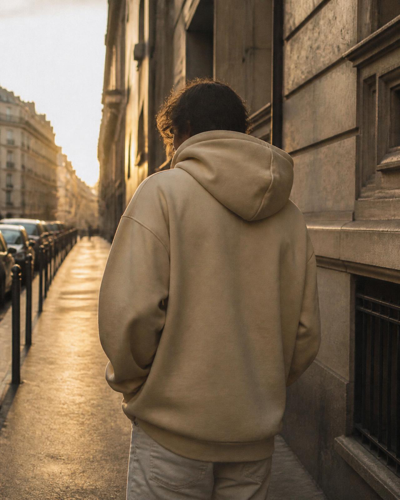 Person walking a golden-hour street in a sand-coloured hoodie